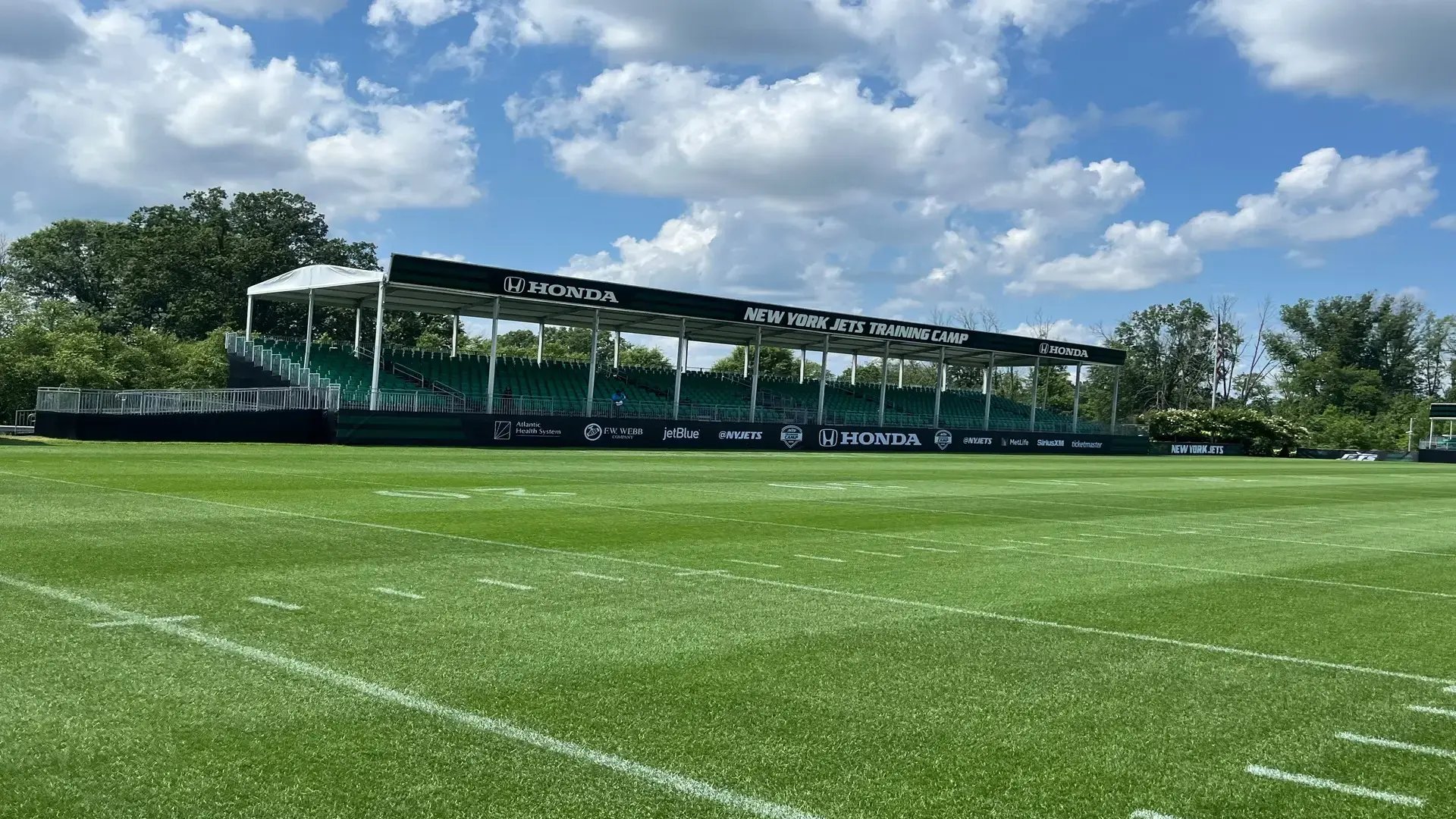 “InProduction single-level on-field hospitality structure with elevated seating platforms installed for New York Jets training camp, giving fans an up-close view of practice.