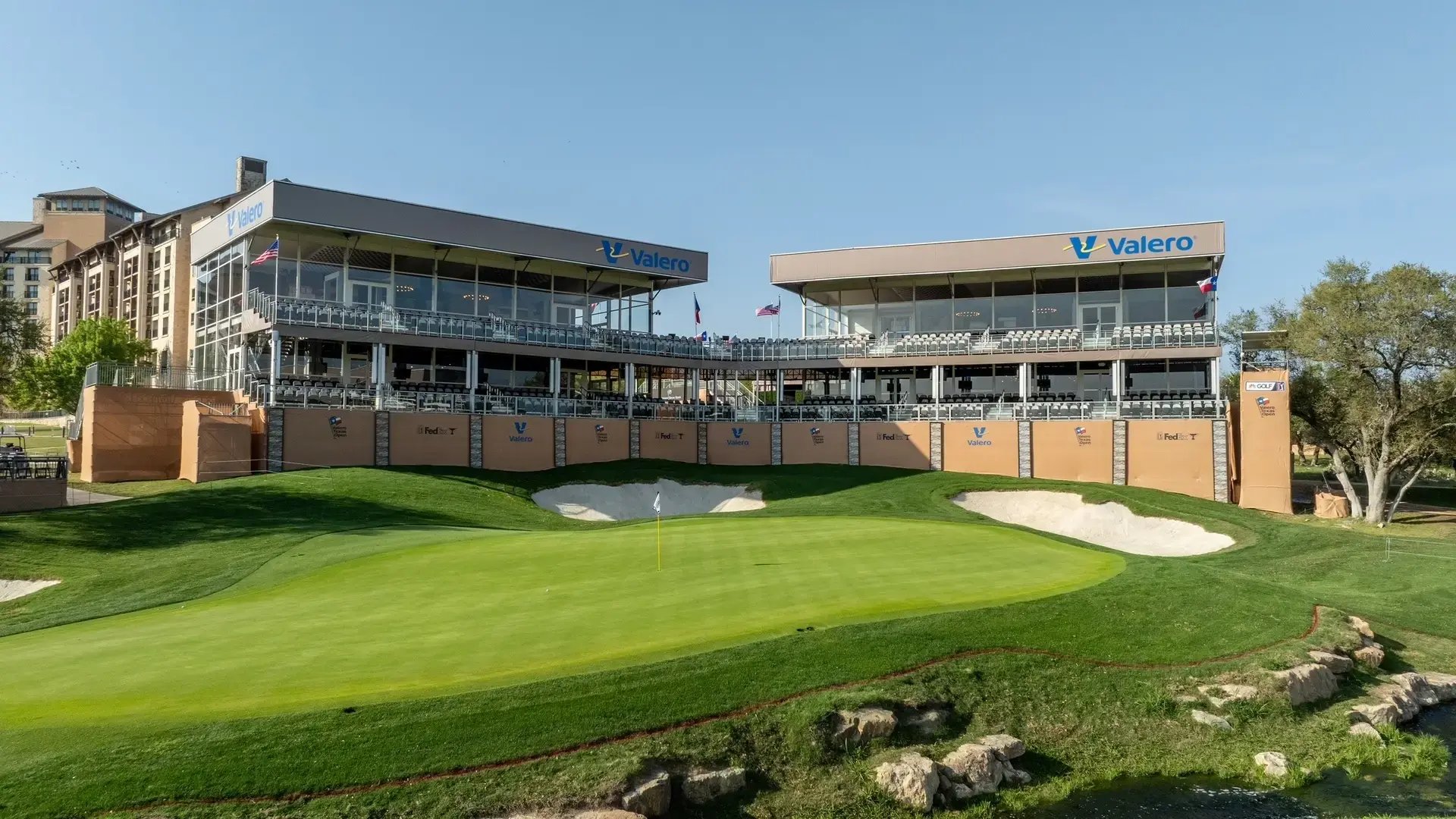InProduction double-deck hospitality structure with custom mesh branding installed for the Valero Texas Open, providing shaded suites and elevated fairway views.